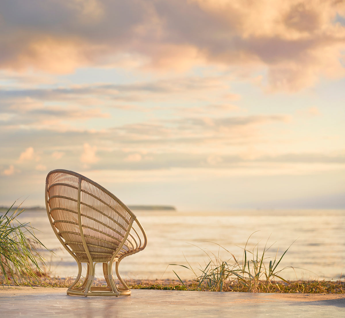 Dies ist ein Lifestyle-Bild von Luna Außen-Lounge-Sessel in natural aluminium artfibre. Von hinten an einem Strand bei Sonnenuntergang mit pastellfarbenem Himmel gesehen.