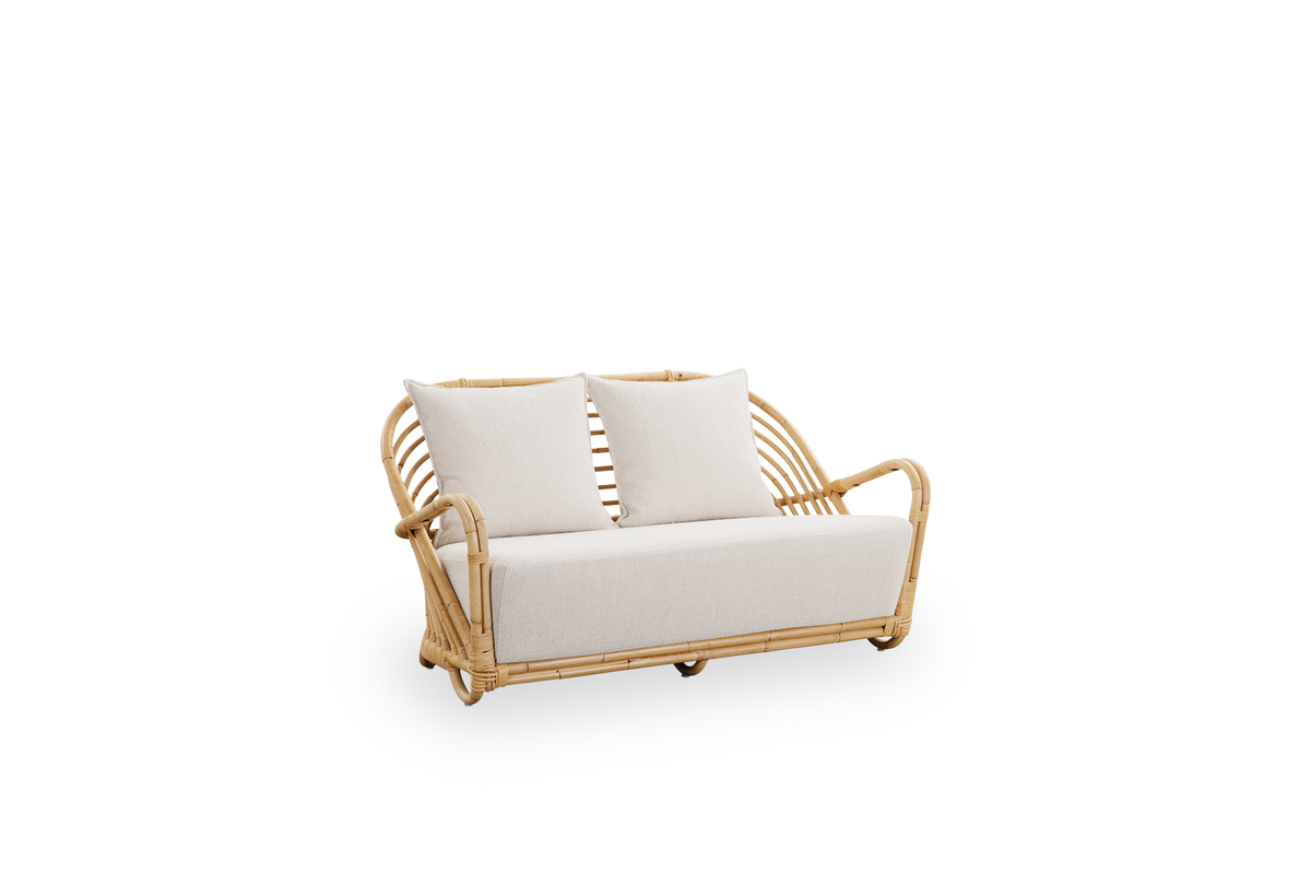 Seitenansicht des Charlottenborg 2-Sitzer-Sofas aus poliertem Natur-Rattan, entworfen von Arne Jacobsen. Das Sofa verfügt über eine gebogene Rückenlehne und in die Basis integrierte Armlehnen, handgefertigt aus hochwertigem indonesischem Rattan.