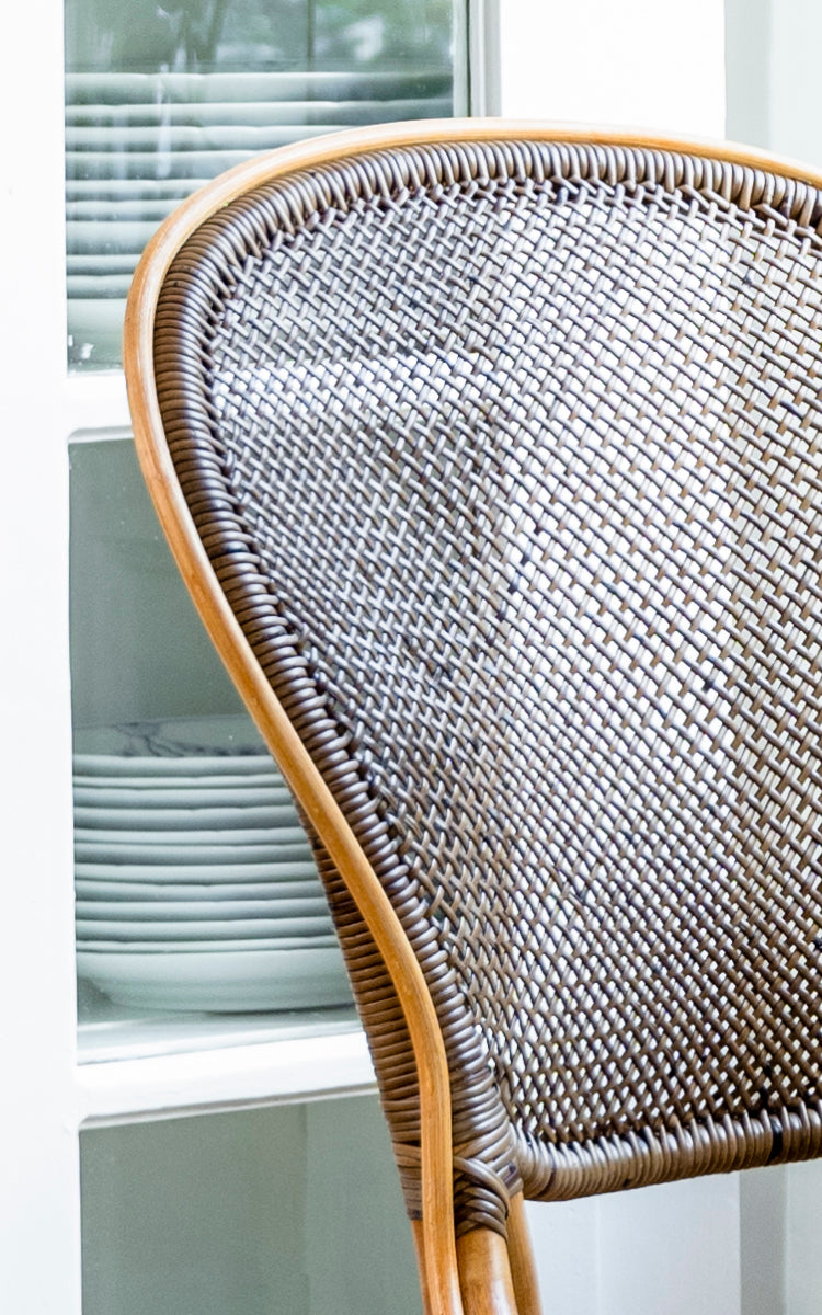 Dies ist ein Nahaufnahmebild von Rossini Esszimmerstuhl in cherry rattan. Detailansicht der dunklen Kirsch-Korbgeflecht-Rückenlehne vor hellen Schränken.
