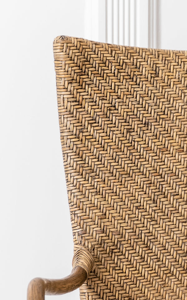 Dies ist ein Nahaufnahmebild von Melody Dining Armchair i antique rattan. Detail der Fischgrätgeflecht-Rückenlehne und der gebogenen Rattan-Armlehne.