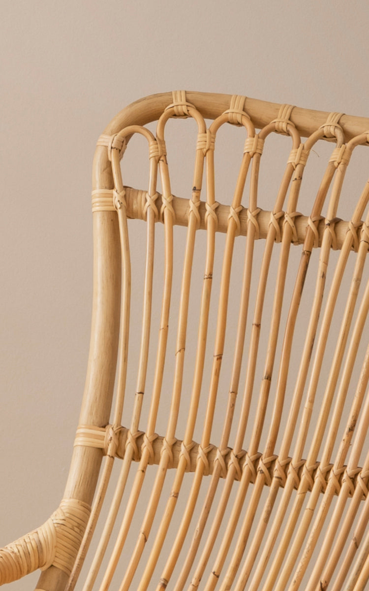 Dies ist ein Nahaufnahmebild von Monet Rocking Chair i natural rattan. Detail des Schlaufenbogen-Designs und der umwickelten Rattanbindung oben.