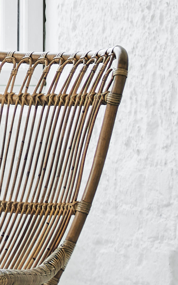 Dies ist ein Nahaufnahmebild von Monet Lounge Chair i antique rattan. Detail der Schlaufenbogen-Rückenlehne mit vertikalen Stäben und geflochtenem Sitz.