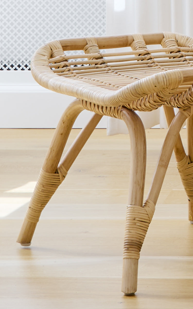 Dies ist ein Nahaufnahmebild von Monet Footstool i natural rattan. Detail des flachen geflochtenen Sitzes und der umwickelten Rattanverbindungen an den Beinen.