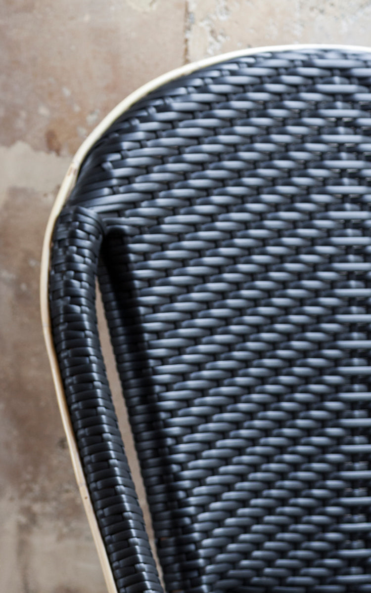 Dies ist ein Nahaufnahmebild von Sofie Esszimmerstuhl in black artfibre skin on rattan frame. Detail der geflochtenen Textur und Rahmenkonstruktion.