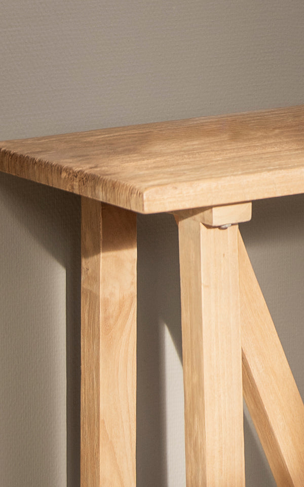 Dies ist ein Nahaufnahmebild von Lucas Teak Konsolentisch in teak indoor. Die massive Teakoberfläche und die gewinkelten Bockbeine zeigen klare Linien und Holztöne.