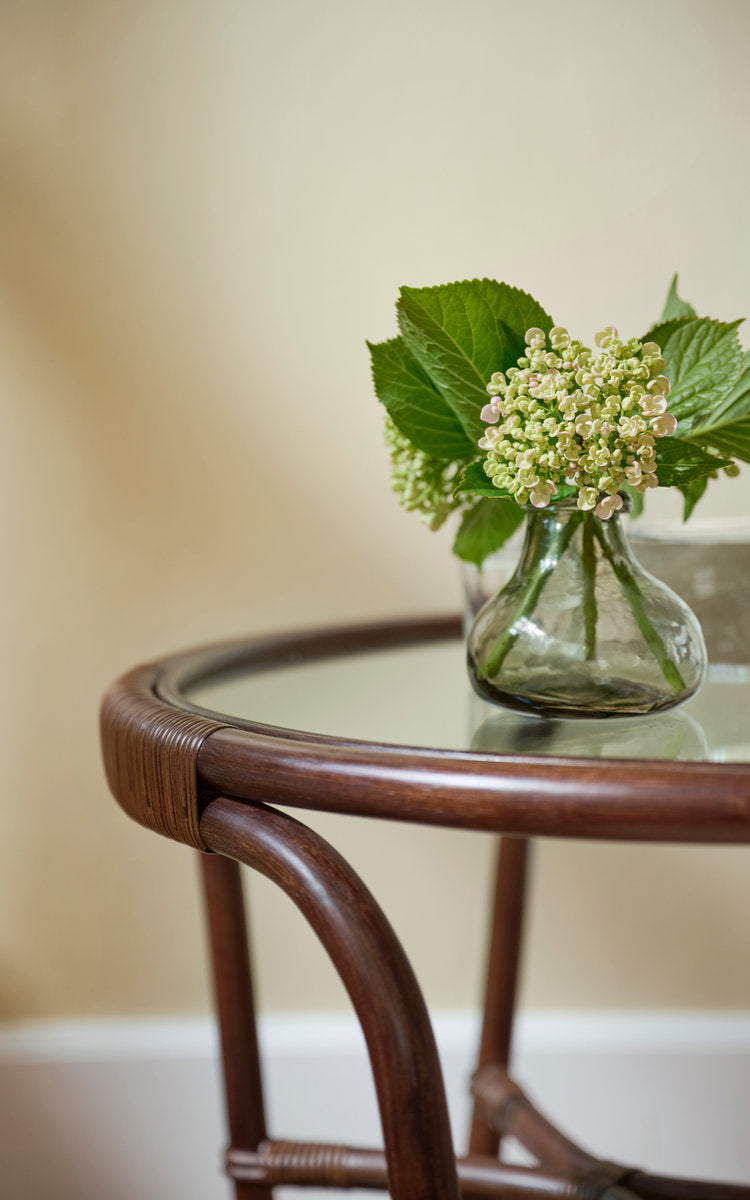 Dies ist ein Nahaufnahmebild von Charlottenborg Couchtisch in brown rattan. Glasplatte und Rattangestell mit Hortensienvase.