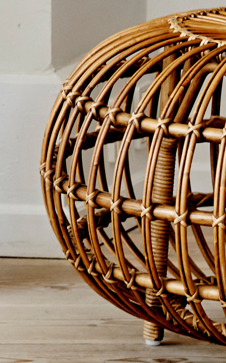 Dies ist ein Nahaufnahmebild von Ottoman Large in polished antique rattan. Detail des großen offenen Rattankäfigs mit gebogenen Rippen auf Holzboden.