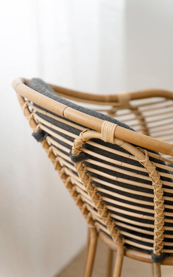 Dies ist ein Nahaufnahmebild von Swing Lounge-Sessel in polished natural rattan. Detail der geschwungenen Rattan-Oberleiste und der geflochtenen Rückenlehnenbindung.