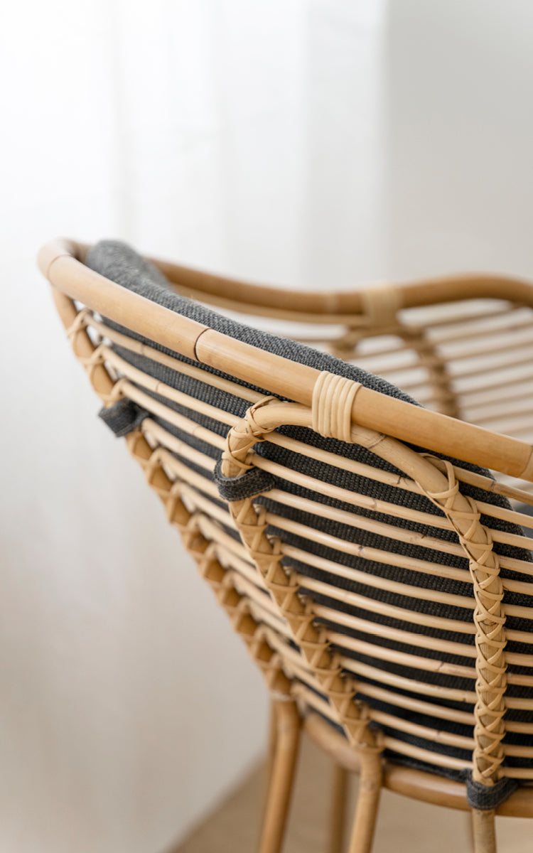Dies ist ein Nahaufnahmebild von Swing Lounge-Sessel in polished natural rattan. Detail der geschwungenen Rattan-Oberleiste und der geflochtenen Rückenlehnenbindung.