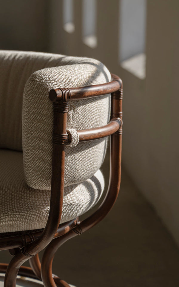 Dies ist ein Nahaufnahmebild von Coco Lounge-Sessel in brown rattan. Umwickelte Armlehne und weiches Kissen im Tageslicht.