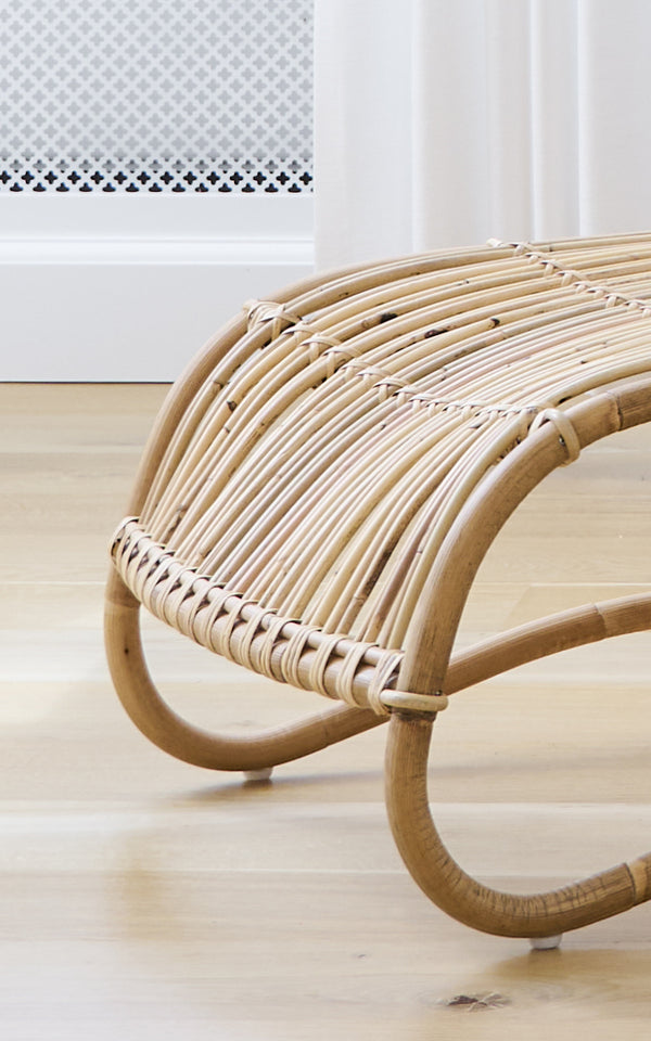 Dies ist ein Nahaufnahmebild von Teddy Fußhocker in polished natural rattan. Detail der gebogenen Rattanleisten und der geflochtenen Umwicklung des Fußhockers.