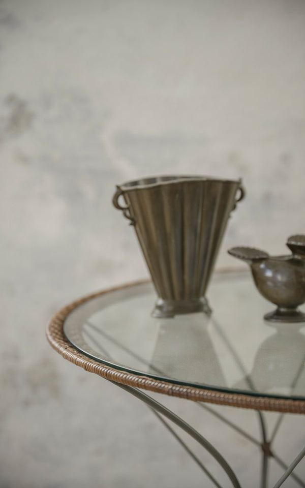 Dies ist ein Nahaufnahmebild von Funky Cafétisch in hazelnut rattan iron frame. Glasplatte mit Zinnvase und Krug.