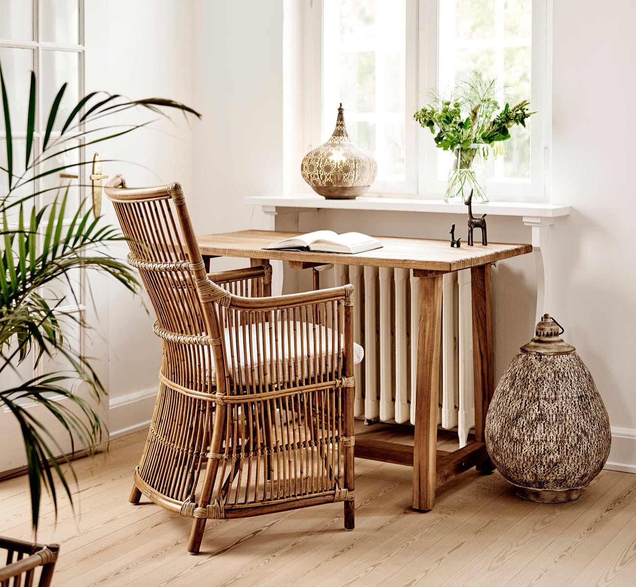 Dies ist ein Lifestyle-Bild von Davinci Esszimmerstuhl in antique rattan, in einem hellen Interieur mit weißen Wandpaneelen und Fischgrätparkett.