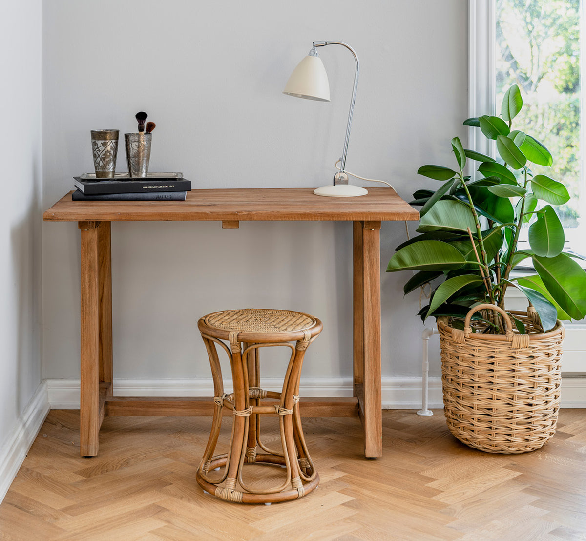 Dies ist ein Lifestyle-Bild von Bella Hocker in antique rattan, in einem hellen Interieur mit weißen Wandpaneelen und Fischgrätparkett.