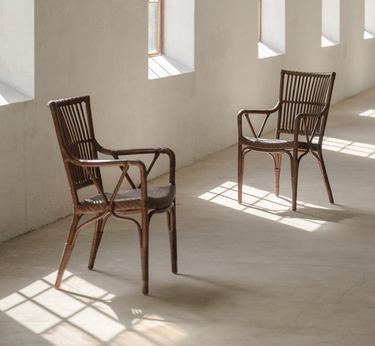 Dies ist ein Lifestyle-Bild von Piano Esszimmerstuhl in brown rattan. Paar in einem sonnigen Raum mit Betonboden.