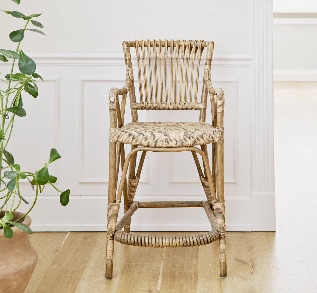 Dies ist ein Lifestyle-Bild von Blues Barstuhl in antique Rattan, in einem hellen Interieur mit weißen Wandpaneelen und Fischgrätparkett.