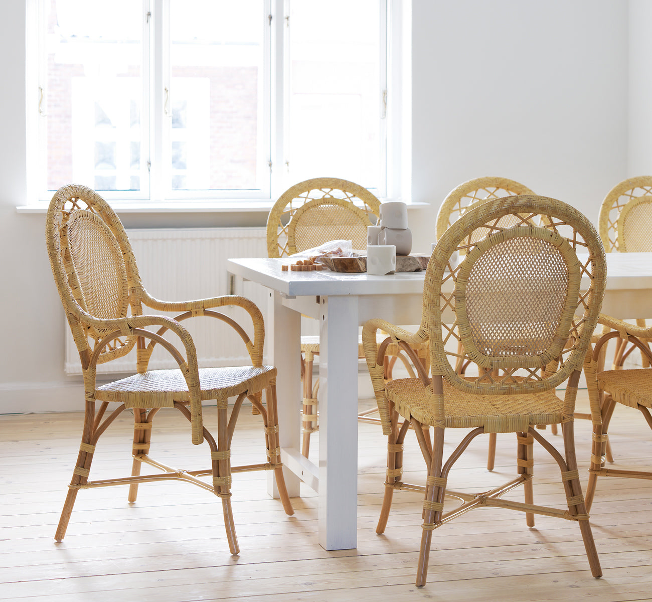 Dies ist ein Lifestyle-Bild von Romantica Esszimmerstuhl in natural rattan. Um einen weißen Esstisch in einem hellen skandinavischen Raum versammelt.