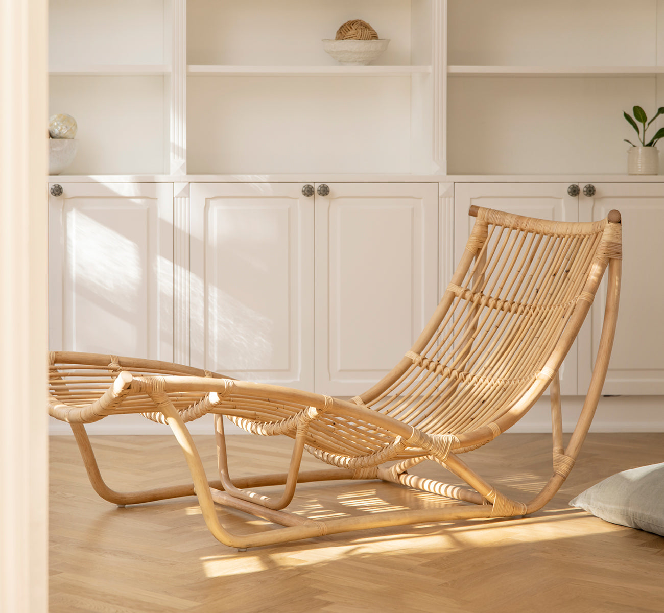 Dies ist ein Lifestyle-Bild von Michelangelo Daybed i natural rattan. Platziert in einem hellen weißen Raum mit Betonboden und rosa Lampe.