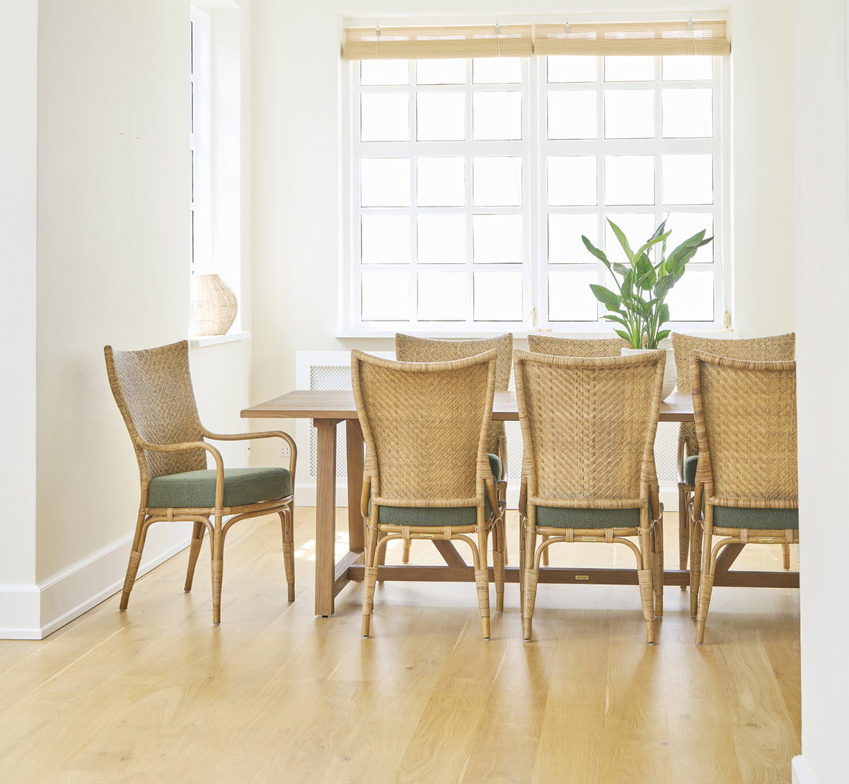 Dies ist ein Lifestyle-Bild von Melody Dining Armchair i antique rattan. Sechs Stühle an einem Teaktisch in einem hellen Raum mit Eichenboden.