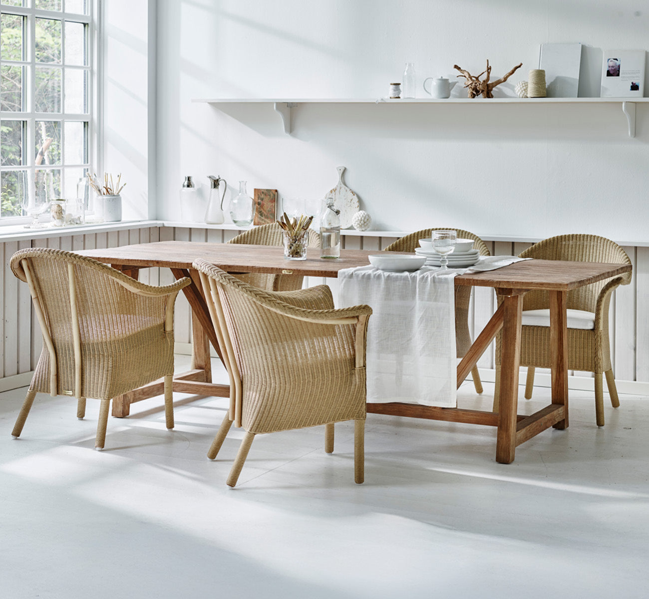 Dies ist ein Lifestyle-Bild von Classic Esszimmerstuhl in natural Loom Rattan Frame, in einem hellen Interieur mit weißen Wandpaneelen und.