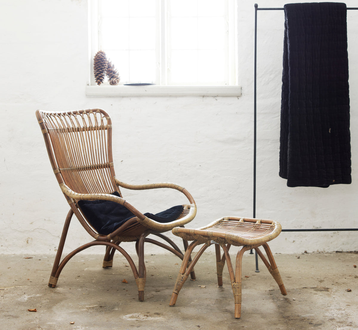 Dies ist ein Lifestyle-Bild von Monet Lounge Chair i antique rattan. Mit Fußhocker und Beistelltisch in einem dunklen rustikalen Scheunen-Setting.