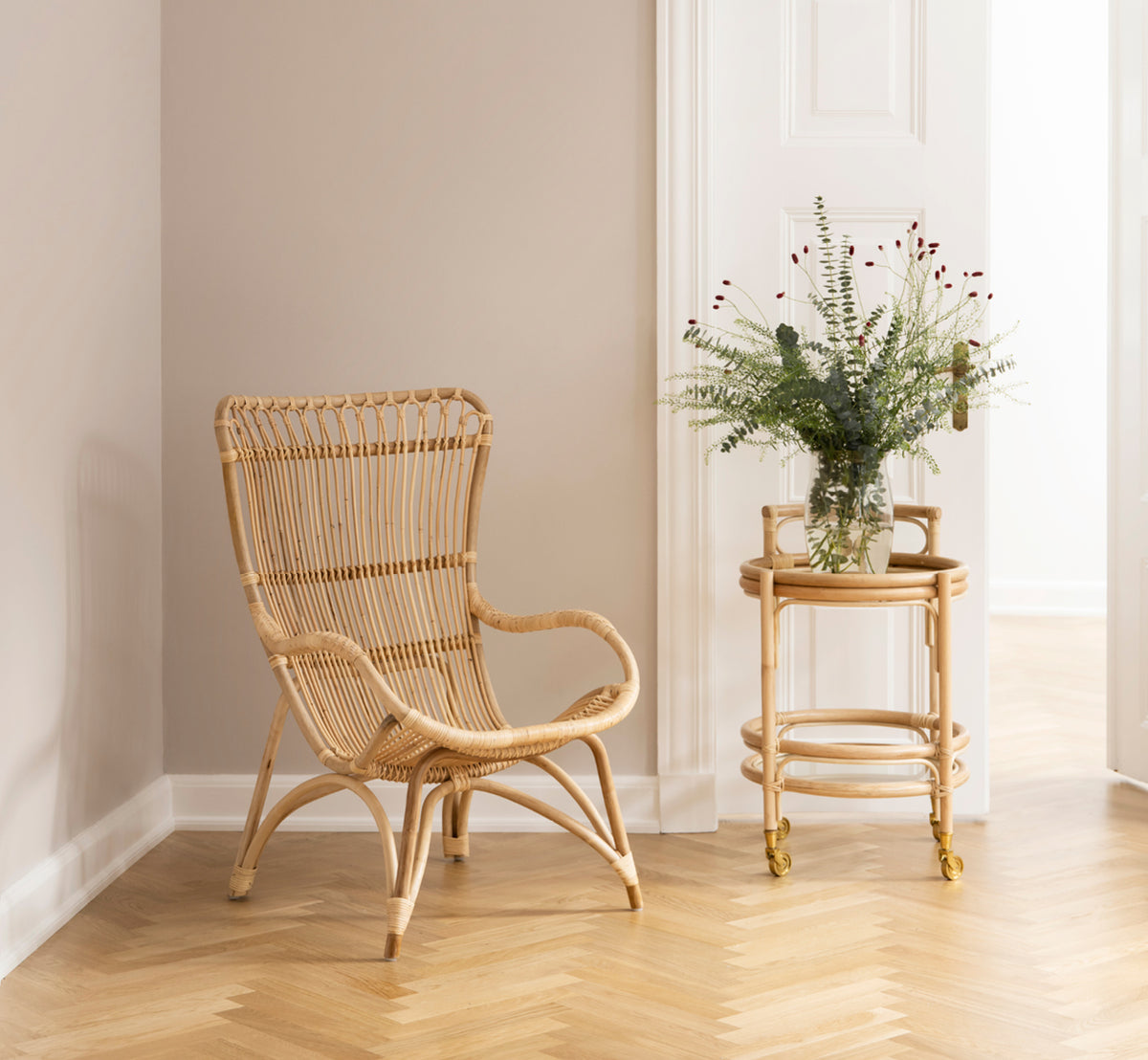 Dies ist ein Lifestyle-Bild von Monet Lounge Chair i natural rattan. Mit Fußhocker und Beistelltisch in einer dunklen rustikalen Scheune mit Kerze.