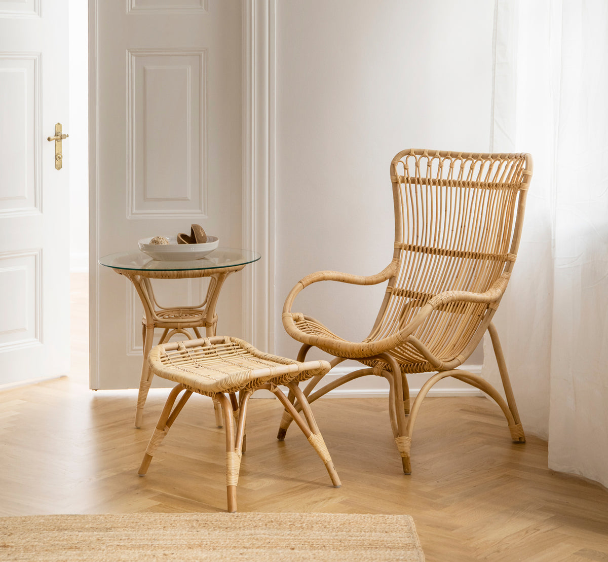 Dies ist ein Lifestyle-Bild von Monet Fußhocker in natural rattan. Mit einem hochlehnigen Rattansessel und Glas-Beistelltisch in einem hellen Eingang kombiniert.