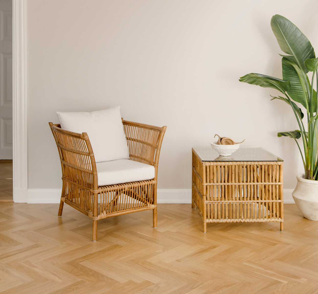 Dies ist ein Lifestyle-Bild von Donatello Lounge-Sessel in antique rattan, in einem hellen Wohnzimmer mit Fischgrätparkett und üppigem Grün.