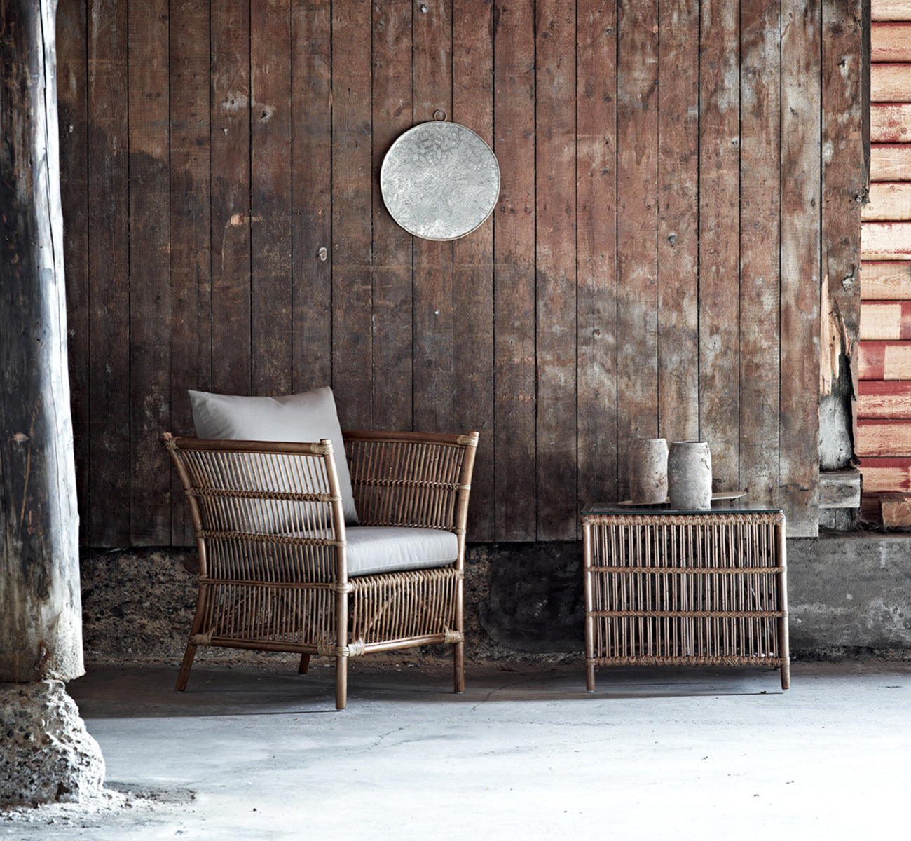 Dies ist ein Lifestyle-Bild von Donatello Lounge-Sessel in antique rattan, in einem hellen Wohnzimmer mit Fischgrätparkett und üppigem Grün.