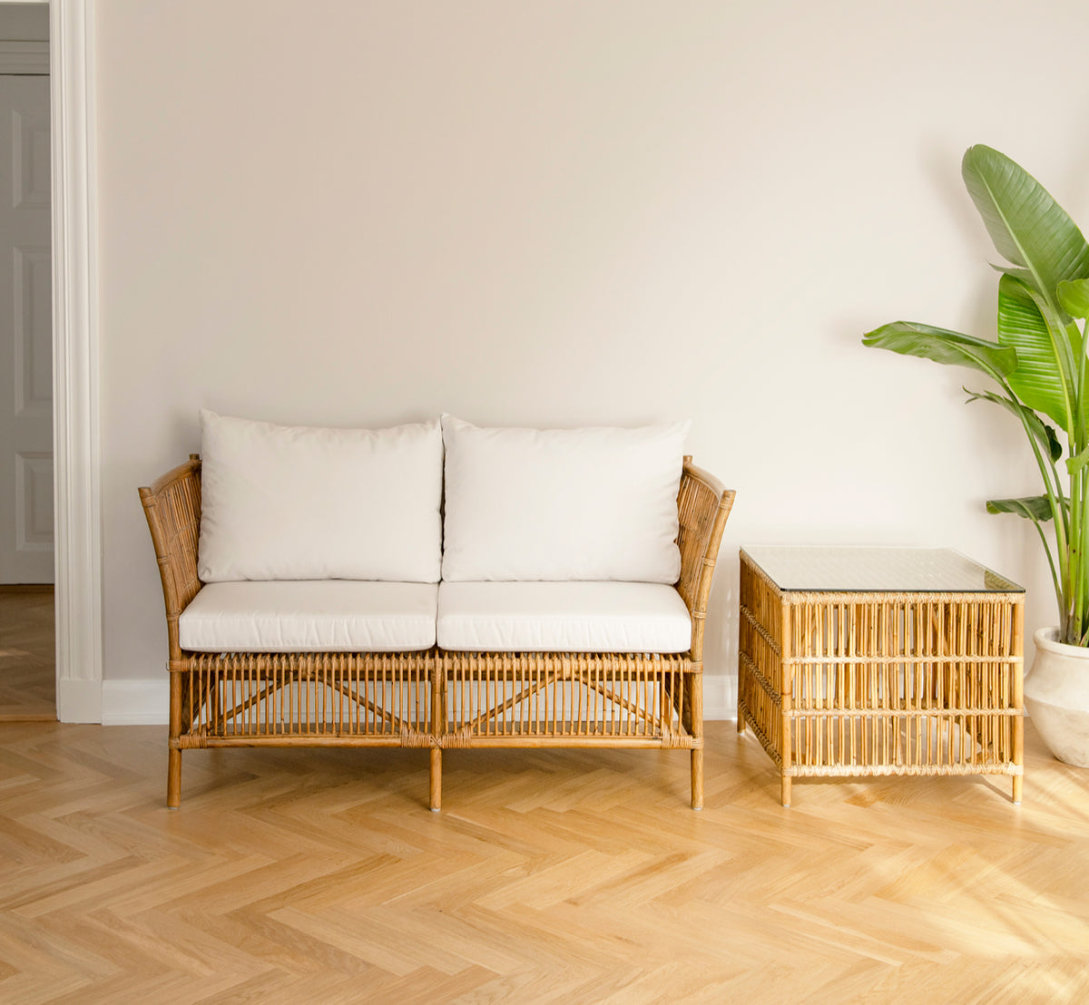 Dies ist ein Lifestyle-Bild von Donatello 2-Sitzer-Sofa in antique rattan, in einem minimalistischen hellen Interieur mit Fischgrätparkett und einer.
