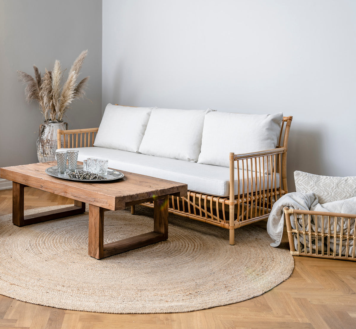 Dies ist ein Lifestyle-Bild von Caroline Sofa in natural rattan, in einem hellen Interieur mit weißen Wandpaneelen und Fischgrätparkett.