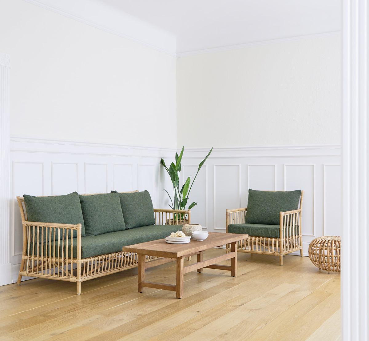 Dies ist ein Lifestyle-Bild von Caroline Sofa in natural rattan, in einem hellen Interieur mit weißen Wandpaneelen und Fischgrätparkett.