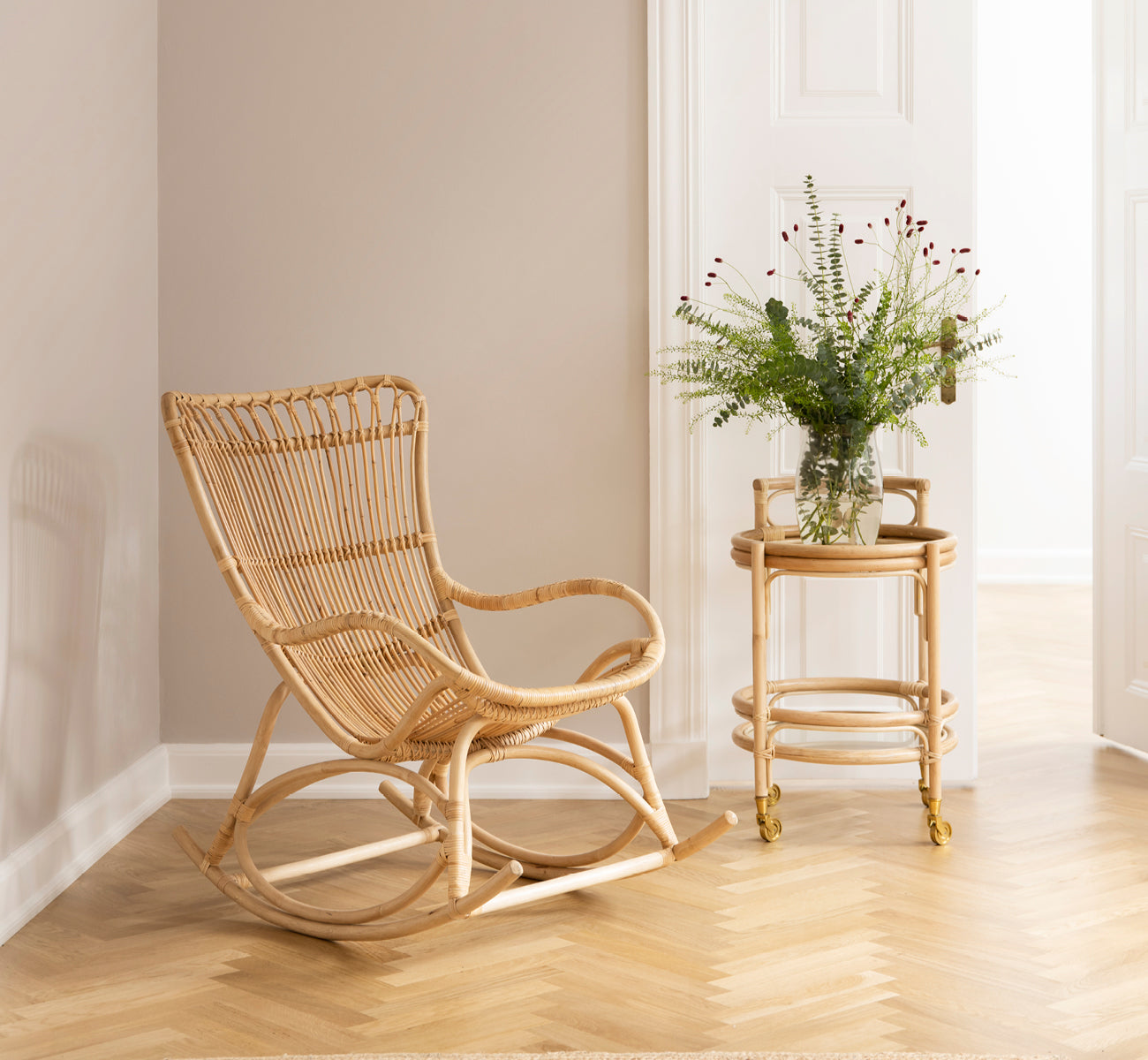 Dies ist ein Lifestyle-Bild von Romeo Trolley i natural rattan. Gestylt mit Gläsern in einer gemütlichen Ecke mit Fischgrätparkett.