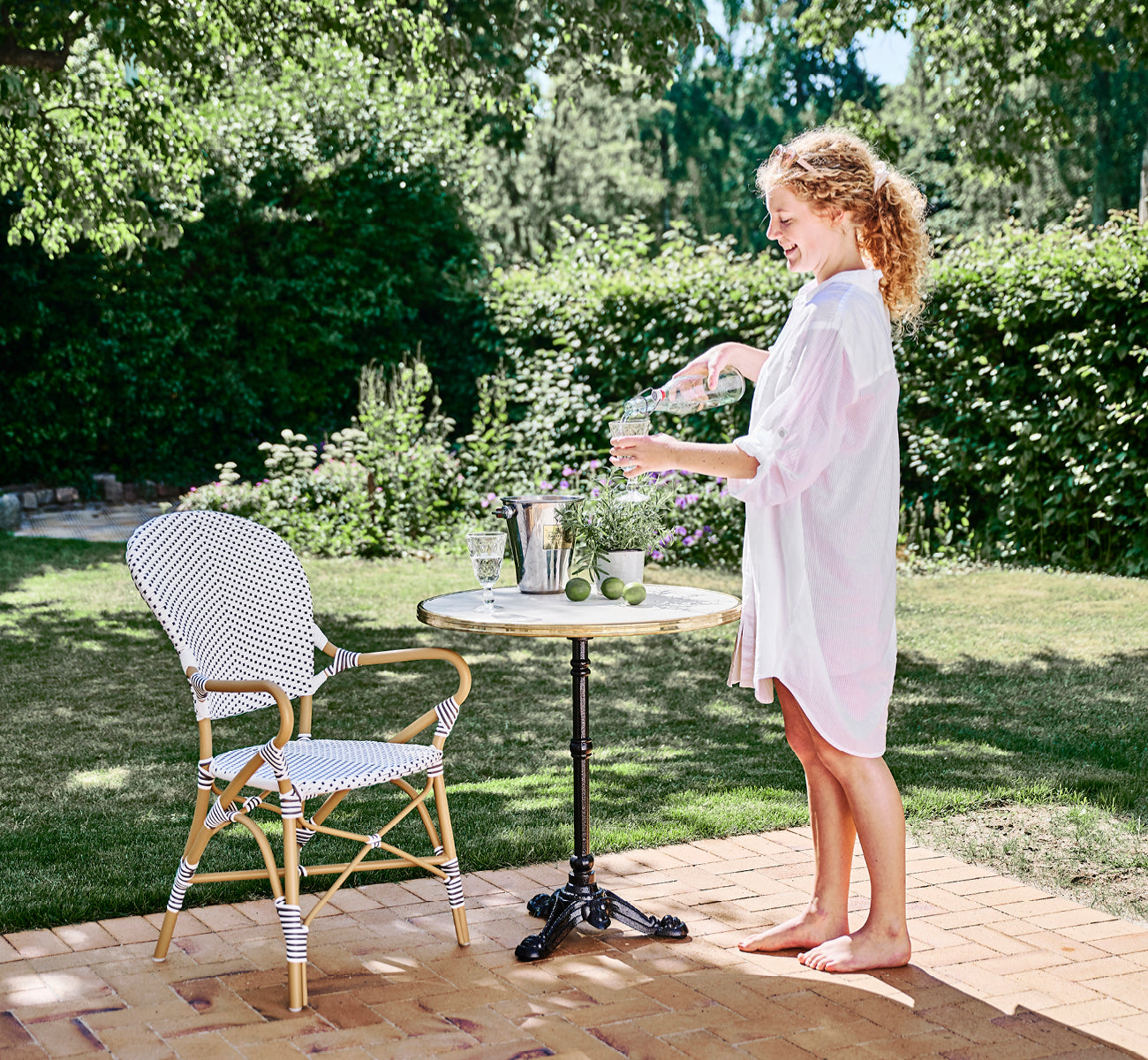 Dies ist ein Lifestyle-Bild von Isabell in almond aluminium frame White w cappuccino dot ArtFibre, auf einer üppigen Gartenterrasse mit Steinboden.