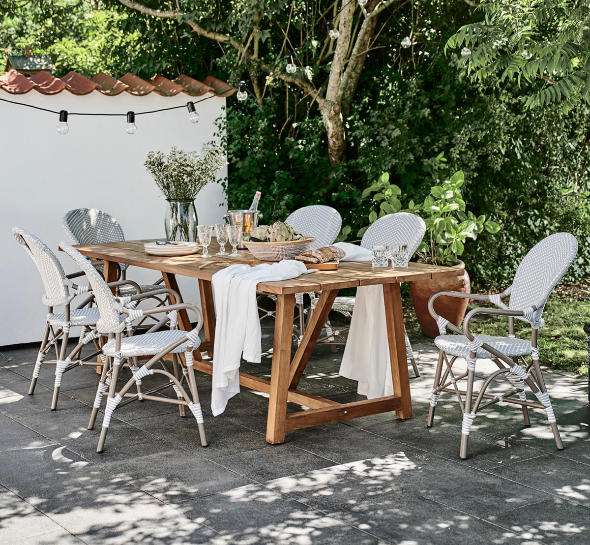 Dies ist ein Lifestyle-Bild von Isabell in taupe aluminium frame Grey w white dot ArtFibre, auf einer üppigen Gartenterrasse mit Steinboden und grün.