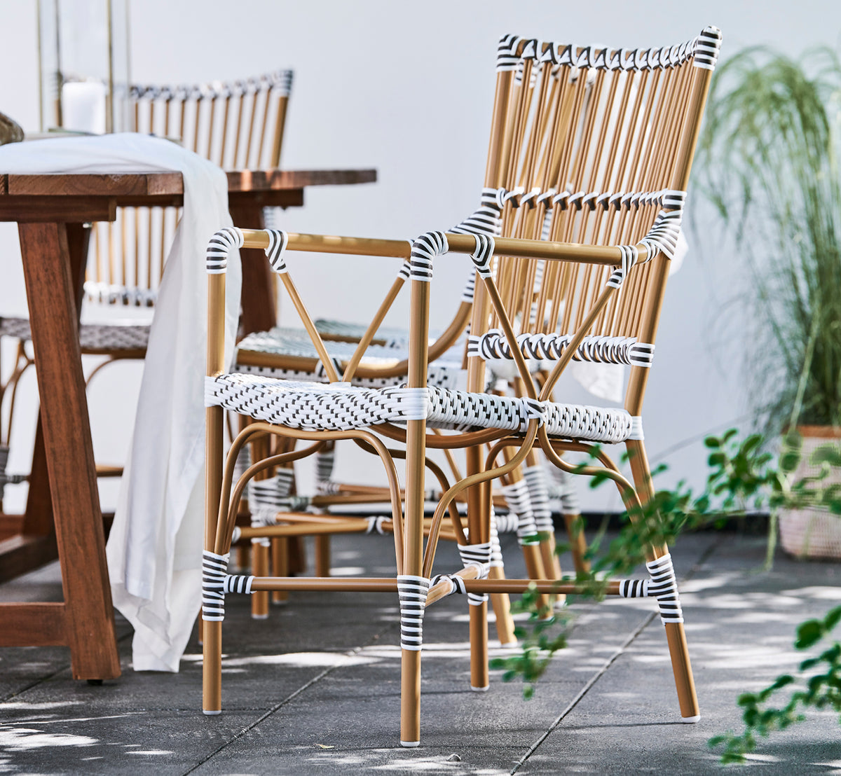 Dies ist ein Lifestyle-Bild von Monique Exterior Dining Armchair i white w cappuccino dot ArtFibre. Auf einer sonnigen Terrasse mit Palmen.
