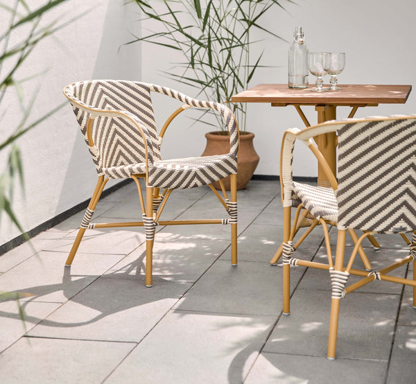 Dies ist ein Lifestyle-Bild von Madeleine Außen-Esszimmerstuhl in almond aluminum frame chevron cappuccino ivory ArtFibre. Sonnige Terrasse mit Teaktisch.