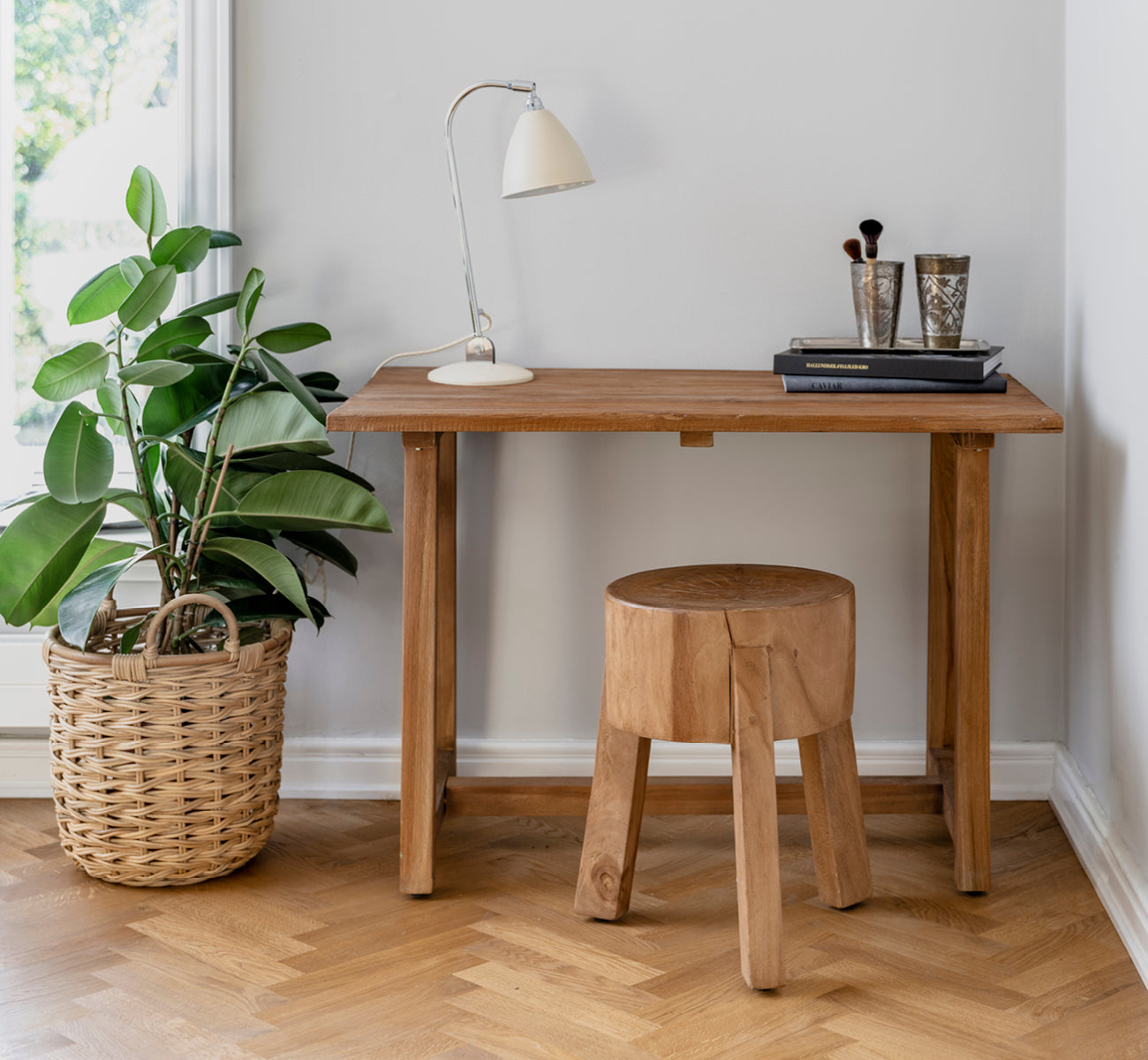 Dies ist ein Lifestyle-Bild von Roger Hocker in teak indoor. An einem Holzschreibtisch mit Lampe und Pflanze in einem hellen Fischgrät-Arbeitszimmer platziert.