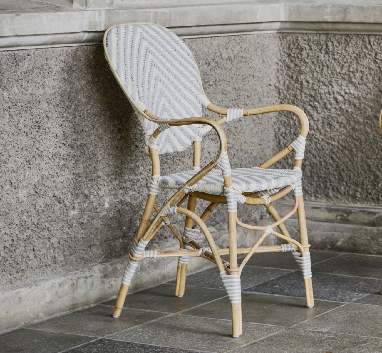 Dies ist ein Lifestyle-Bild von Isabell Esszimmer-Armlehnstuhl in chevron Grey Ivory ArtFibre Skin on Rattan frame, in einem hellen Essbereich mit.