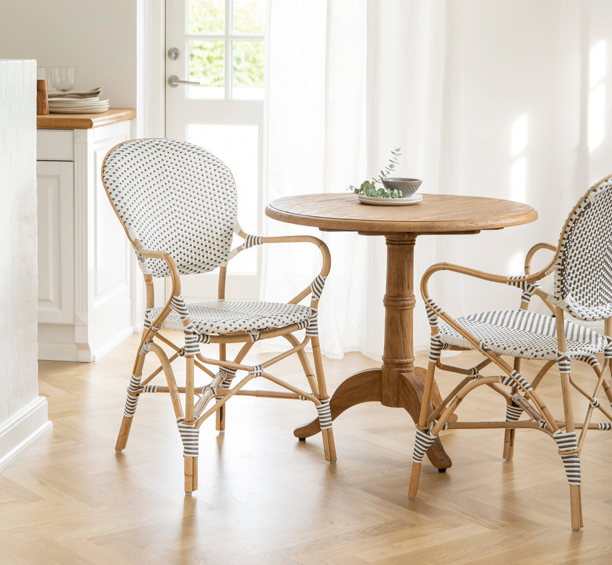 Dies ist ein Lifestyle-Bild von Isabell Esszimmer-Armlehnstuhl in white w cappuccino dot ArtFibre Skin on Rattan frame, in einem hellen Essbereich.