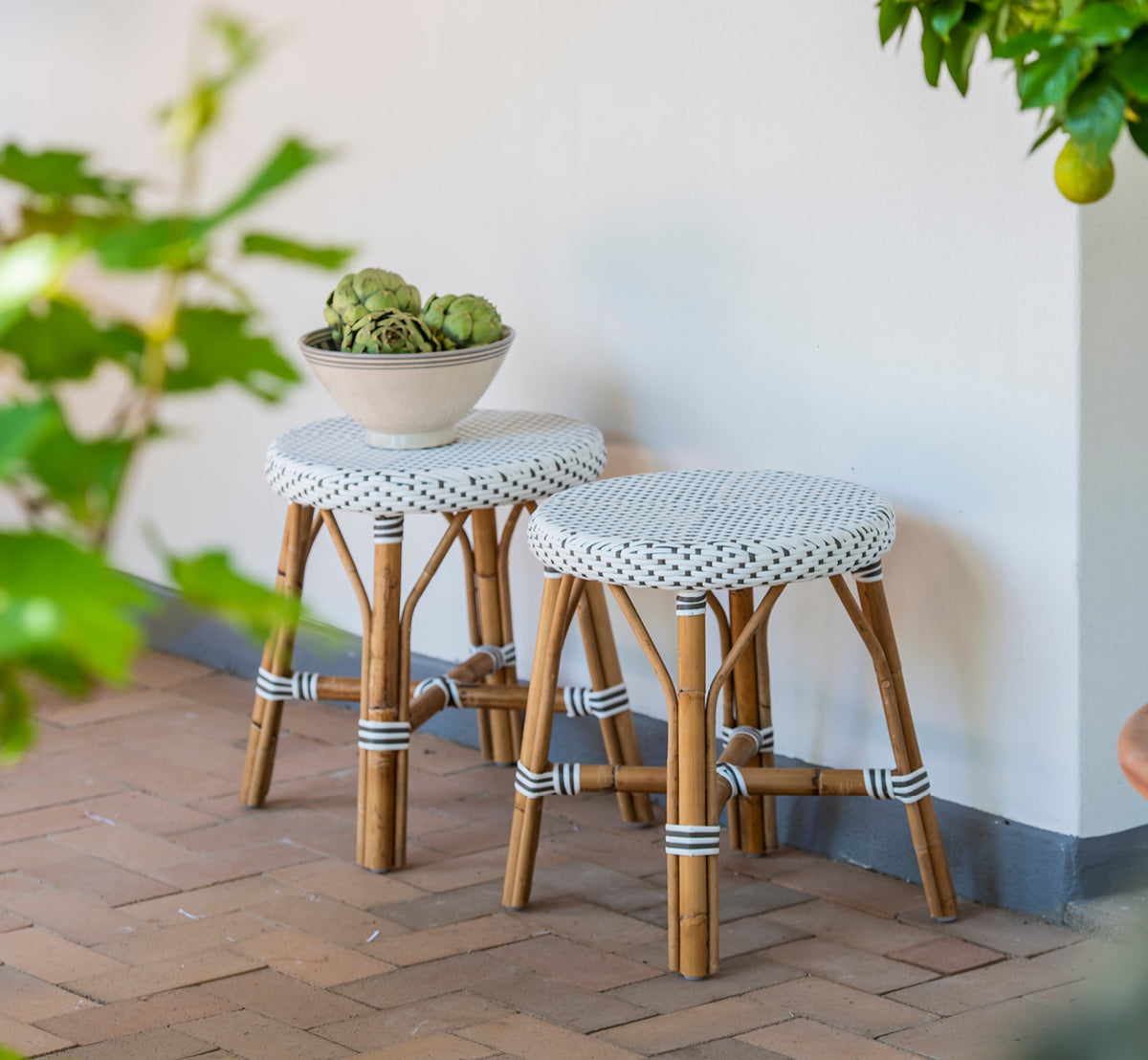 Dies ist ein Lifestyle-Bild von Simone Hocker in white w cappuccino dot ArtFibre Skin on Rattan frame. Ein Paar auf einer Backsteinterrasse.