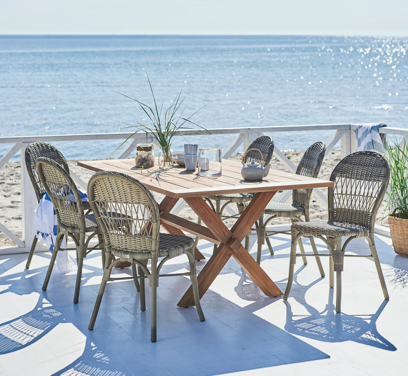 Dies ist ein Lifestyle-Bild von Ofelia Exterior Chair i antique grey artfibre aluminium. Auf einem Stranddeck mit Meerblick und Teekanne.