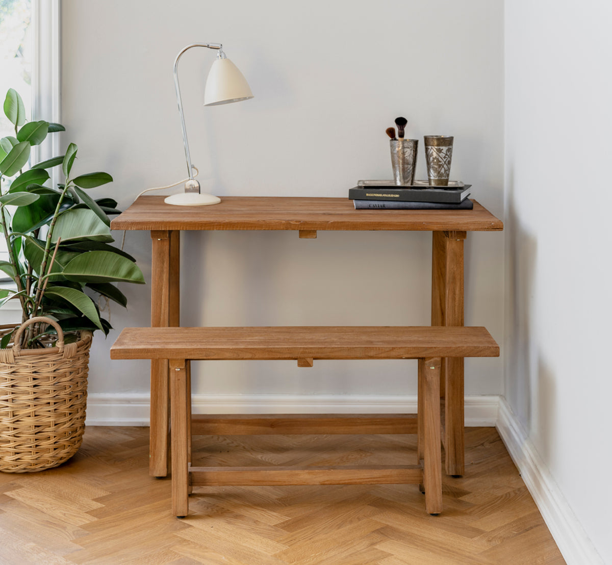 Dies ist ein Lifestyle-Bild von Lucas Teak Bank in teak indoor. Mit einem Teakschreibtisch, Lampe und Büchern in einer gemütlichen Ecke auf Fischgrätboden kombiniert.