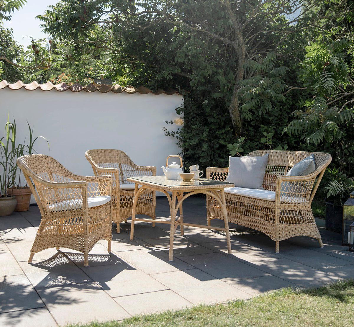 Dies ist ein Lifestyle-Bild von Charlot 2-Sitzer-Sofa in natural ArtFibre Aluminium, auf einer Küstenterrasse mit Schilfdach, Meerblick und.