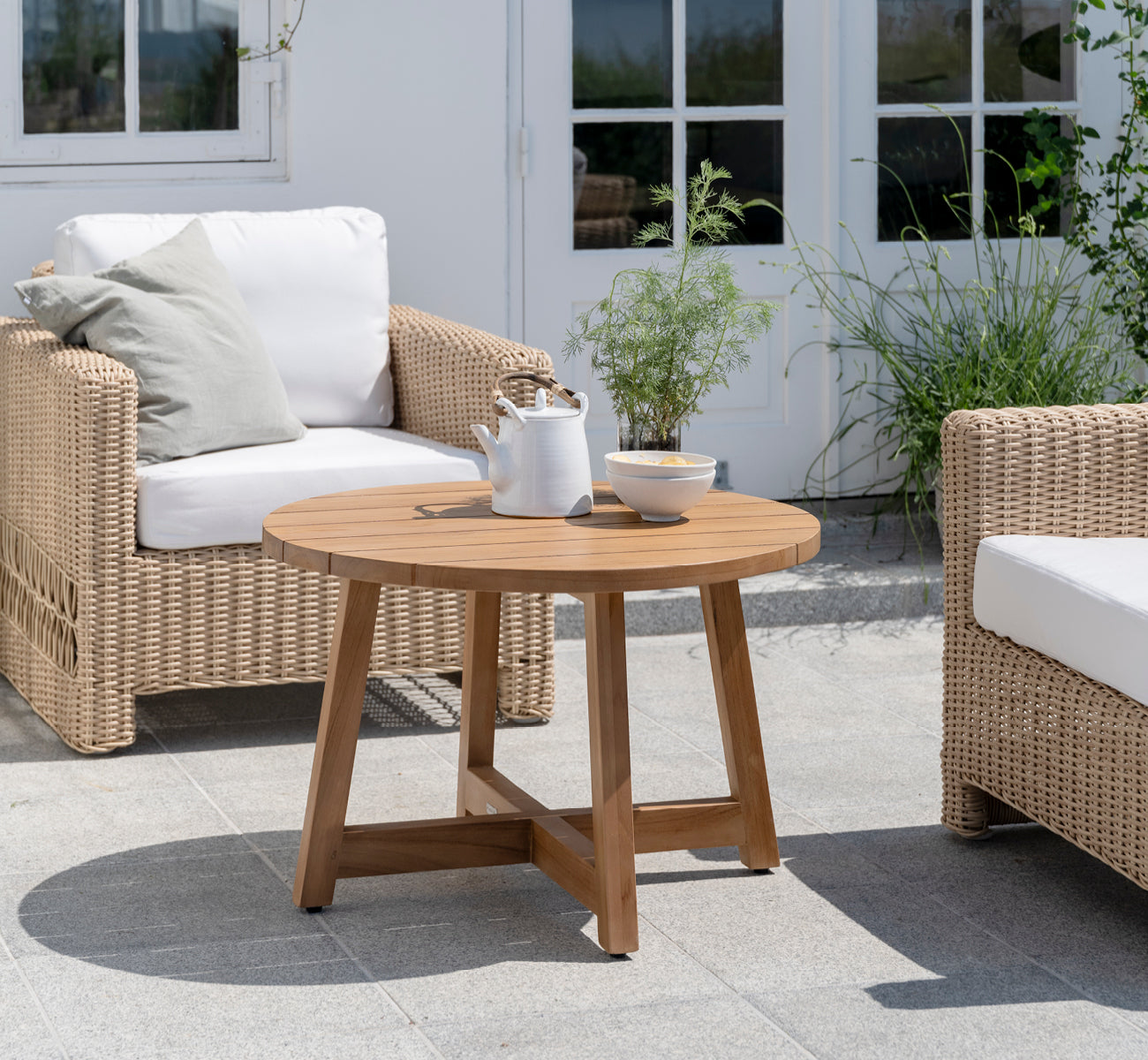 Dies ist ein Lifestyle-Bild von Victor Teak Lounge Table Ø75 cm in teak outdoor. Auf einer Strandterrasse zwischen Tagesbetten mit gestreiften Kissen aufgestellt.