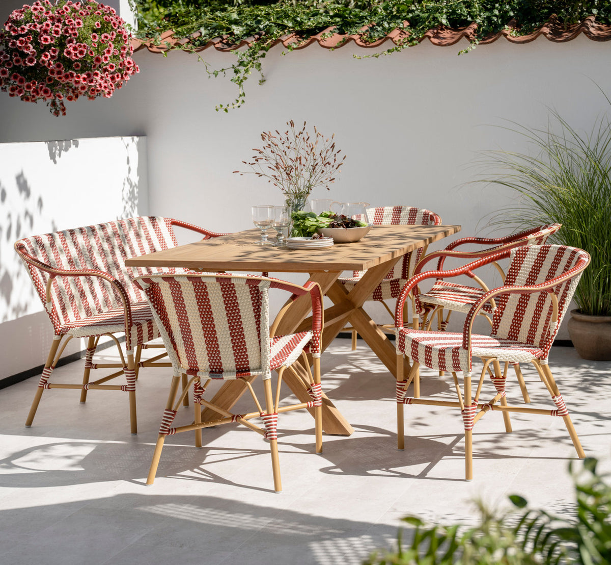 Dies ist ein Lifestyle-Bild von Colonial Teaktisch 160x100 cm in teak outdoor. Mit gestreiften Stühlen auf einer sonnigen, ummauerten Terrasse.