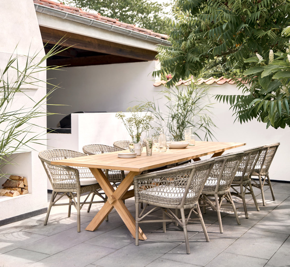 Dies ist ein Lifestyle-Bild von Colonial Tisch 300 in outdoor Teak, auf einer Strandterrasse mit weißem Holzdeck und Meerblick.