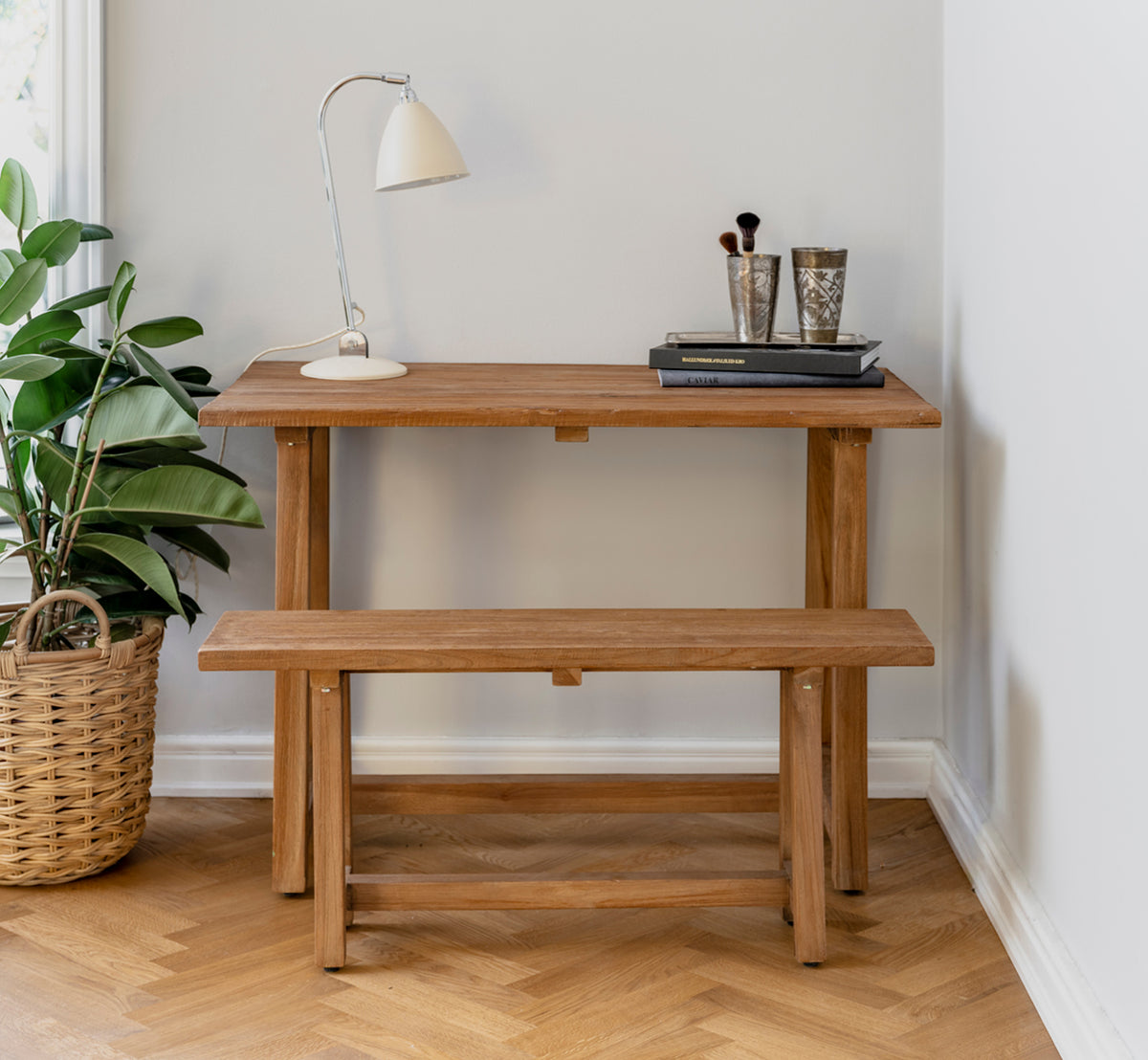 Dies ist ein Lifestyle-Bild von Lucas Teak Schreibtisch in teak indoor. Mit passender Bank, Schreibtischlampe und Büchern in einer gemütlichen Ecke gestylt.