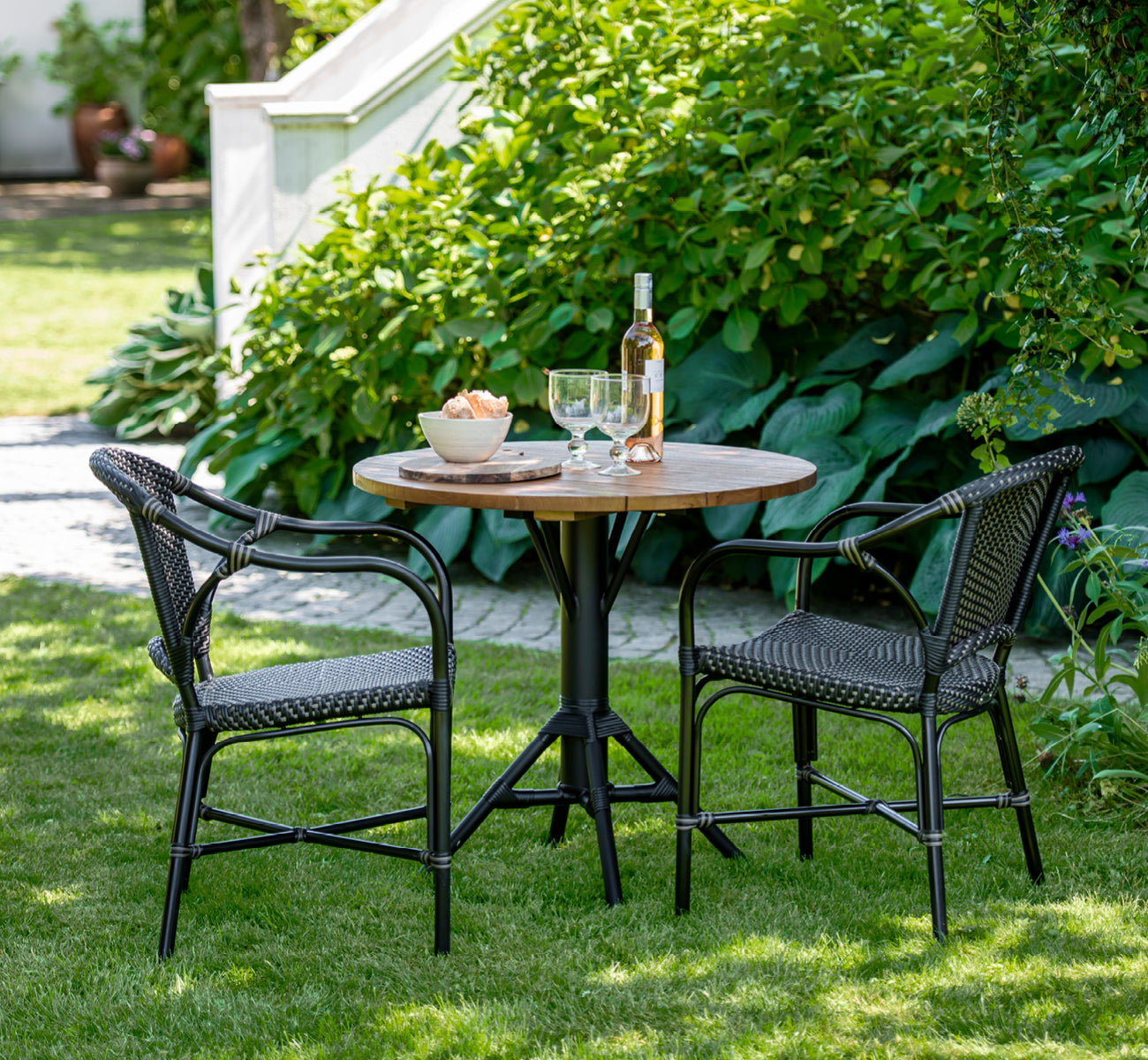 Dies ist ein Lifestyle-Bild von Nicole Cafe Table i black aluminium frame black ArtFibre. Auf einer Steinterrasse mit Gartengrün.