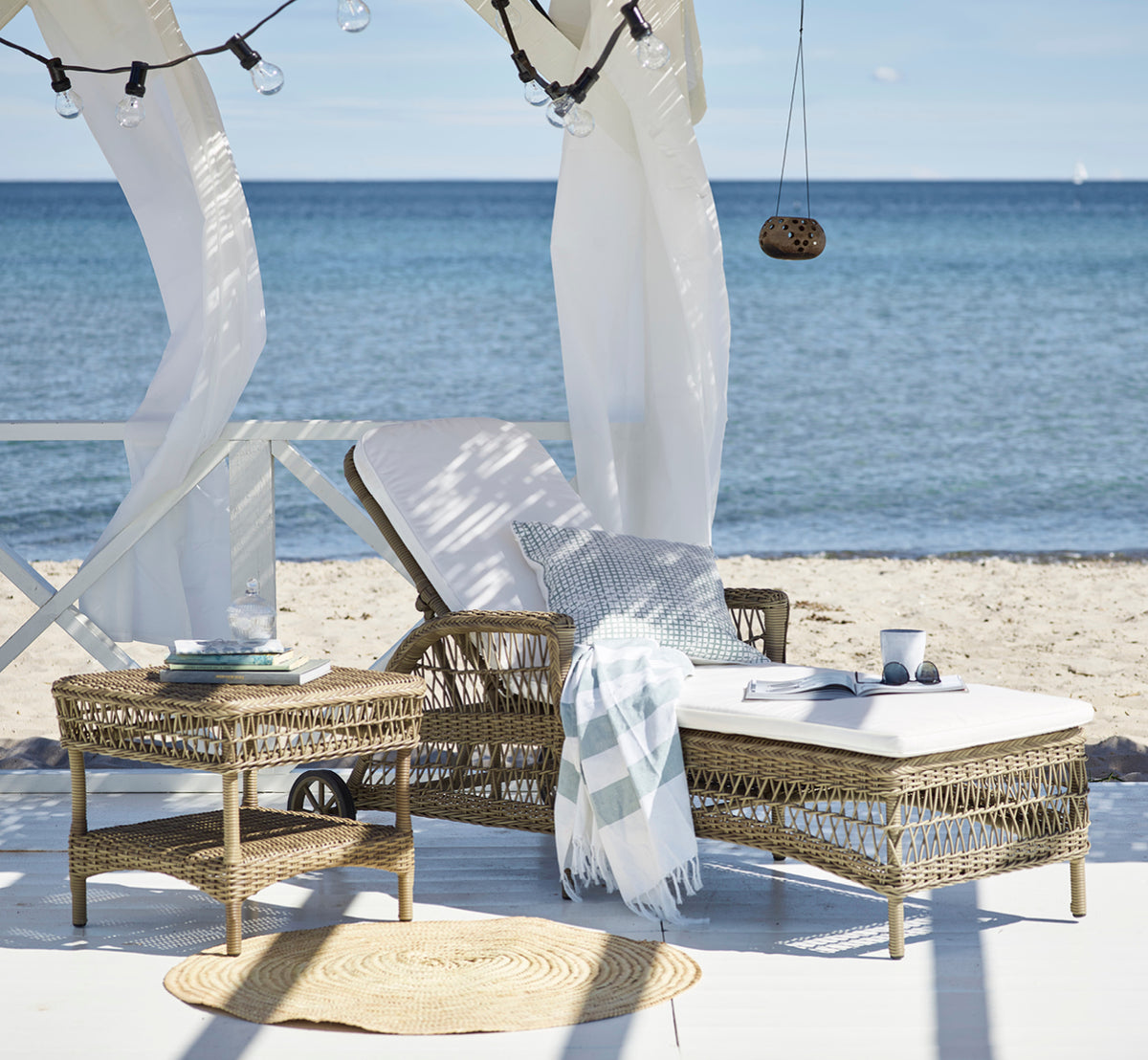 Dies ist ein Lifestyle-Bild von Susy Beistelltisch in antique Grey ArtFibre Aluminium, auf einer Küstenterrasse mit Meerblick, Strandgräsern und.